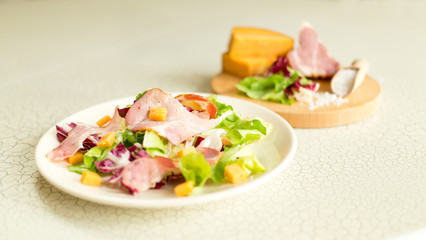 A plate of salad of green leaves, ham and cheese. Plate of salad with green leaves, ham and cheese. Fresh lettuce, cheese, ham and sea salt on a cutting board. Intercontinental breakfast at the hotel.