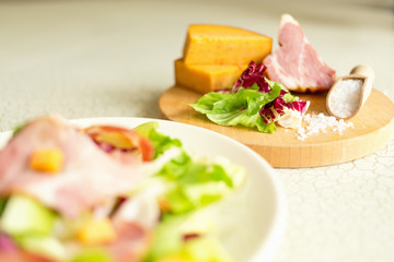 A plate of salad of green leaves, ham and cheese. Plate of salad with green leaves, ham and cheese. Fresh lettuce, cheese, ham and sea salt on a cutting board. Intercontinental breakfast at the hotel.