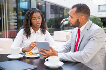 Multiethnic business colleagues watching and discussing content on tablet. Business man and woman sitting in cafe, using tablet together and talking. Wi-Fi concept