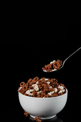 white bowl with assorted cereal and spoon isolated on black