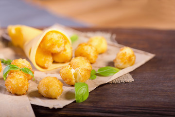 Cheese balls with basil leaves on a wooden table. Cheese snacks for beer.