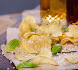 Potato chips with salt and greens on a table in a pub on a background of beer. Chips with greens as a snack to beer. October Beer Fest.