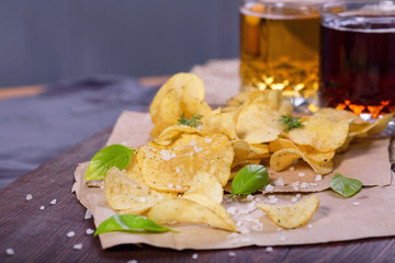 Potato chips with salt and greens on a table in a pub on a background of beer. Chips with greens as a snack to beer. October Beer Fest.