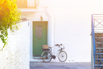 Fototapeta na wymiar Vintage bicycle with basked, against white wall, in narrow street of a small Greek town