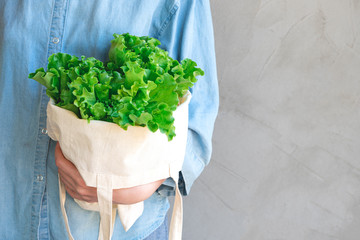Sustainable lifestyle concept. Woman in a blue shirt holds a cotton eco bag with green lettuce....