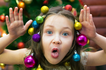 Fototapeta na wymiar Little girl with a garland and Christmas balls in her hair on her head laughing before Christmas. Merry girl on new years eve.