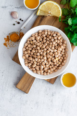 Dry uncooked chickpeas in a bowl, lemon, turmeric, spices, olive oil and coriander on a gray background, top view. Ingredients for cooking chickpeas, Indian cuisine and vegetarian food.
