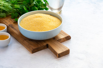 Dry uncooked polenta in a bowl on a cutting board and olive oil, gray background. Traditional italian food, vegetarian food.