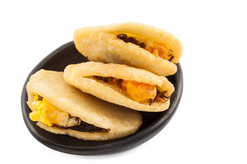 Arepa de huevo. Traditional Colombian fried arepa filled with egg and shredded meat served in a black ceramic dish on white background