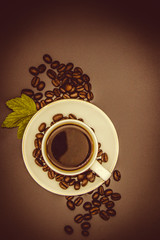 white Cup with black coffee surrounded by roasted coffee beans on a brown background top View