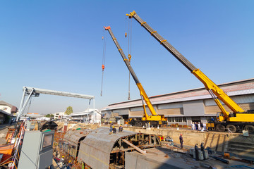 Two truck cranes working over dry dock are lifting ship hull part