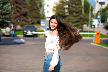 Young beautiful brunette woman in jeans and white blouse walking in summer street