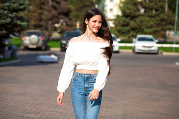 Fototapeta premium Young beautiful brunette woman in jeans and white blouse walking in summer street