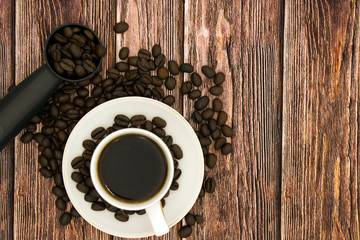 white Cup with black coffee surrounded by roasted coffee beans on a brown background top View