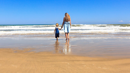 Mom and daughter are walking on the beach. Back view, copy space.