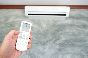 Air conditioner inside the room with woman operating or closing remote controller. / Air...