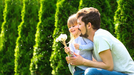Father and daughter blowing dandelion on summer garden. Happy family.