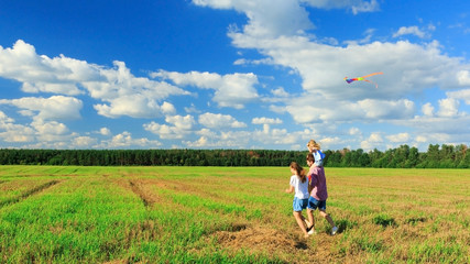 Naklejka na ściany i meble Mother, father and daughter are flying a kite in the field. back view, copy space.