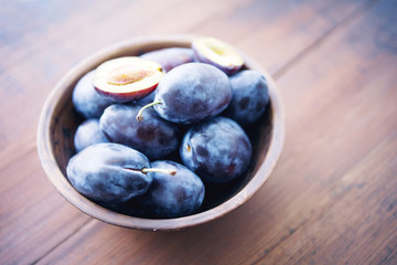 Fresh plums in a bowl on wooden table, soft focus
