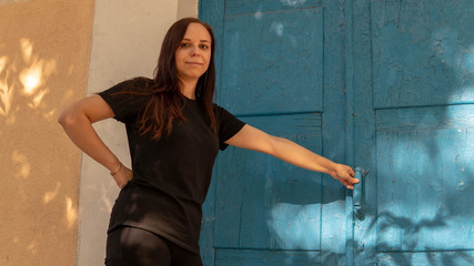 A young woman in a black t-short with long hair on the background of an old building with blue doors.