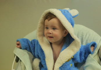 7 months baby in blue terry bathrobe smiles, looks at the camera