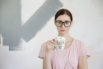 Portrait of a happy young woman holding paint applicator and a cup of coffee or tea, successful house refurbishment concept	