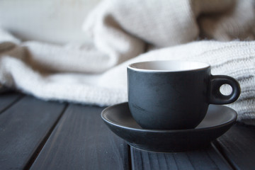 Close-up black cup with coffee on gray knitted sweater made of natural wool texture, wavy folds, selective focus