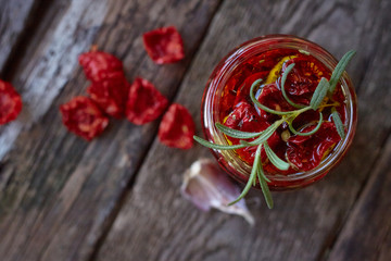 Top view the jar of homemade sun-dried tomatoes with Provencal herbs, garlic and olive oil on a rustic wooden surface, selective focus
