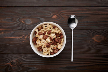 top view of spoon near cereal in bowl on wooden surface