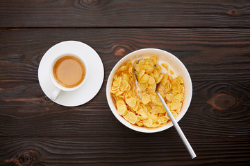 top view of bowl with cornflakes and milk near cup of coffee on wooden surface