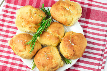 homemade fresh herb bread rolls of Provencal herbs with salt and a sprig branch of rosemary. Bread rolls bakery style on white plate and red and white towel in a cage italian style