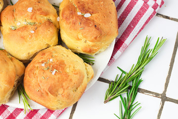 homemade fresh herb bread rolls of Provencal herbs with salt and a sprig branch of rosemary. Bread rolls bakery style on white plate and red and white towel in a cage italian style