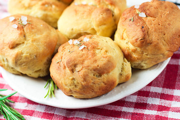 homemade fresh herb bread rolls of Provencal herbs with salt and a sprig branch of rosemary. Bread rolls bakery style on white plate and red and white towel in a cage italian style