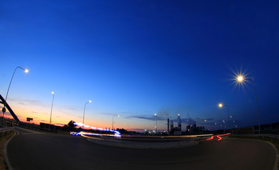 Smugi świateł samochodów na rondzie w nocy po zachodzie słońca, most, elektrownia, błękitne niebo.	 - obrazy, fototapety, plakaty