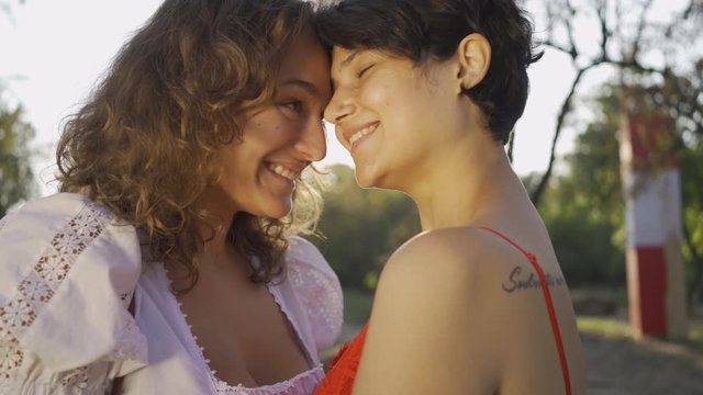 Portrait of two pretty women laughing and rubbing noses close-up. Beautiful lesbian couple enjoying sunset together. Romantic date, love, tender relationship