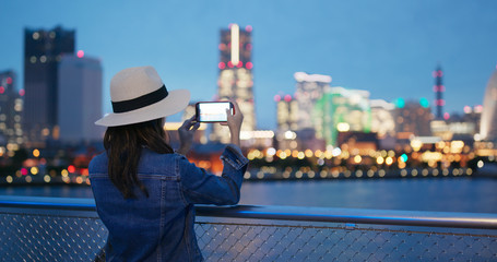Woman take photo on cellphone in city of Yokohama ct night
