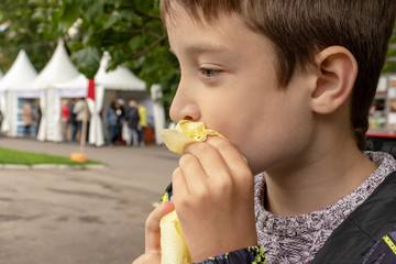 A young caucasian boy sitting in summer city park and wiping his mouse, lips with paper napkin, towel after eating, close up view, takeaway fastfood concept.