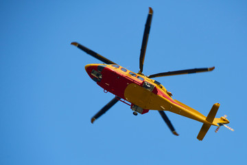 Rescue helicopter moving in blue sky with blur propeller. View from bellow