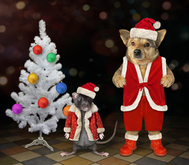 The dog and the pet rat in a Santa Claus outfit is standing next to the Christmas tree in the party.