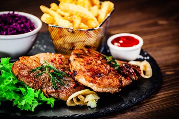 Grilled steak with french fries and vegetables served on black stone on wooden table