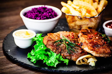 Grilled steak with french fries and vegetables served on black stone on wooden table