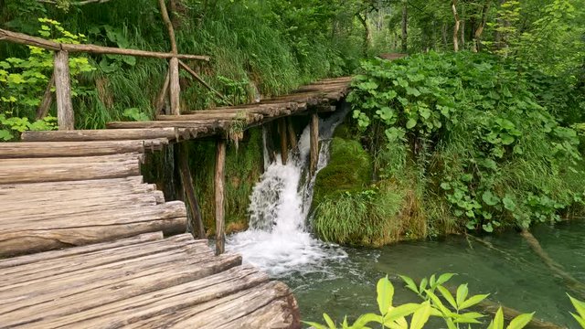 Plitvice Lakes National Park, Croatia. Waterfall flowing into lake under wooden boardwalk among fabulous rich green flora. 4K