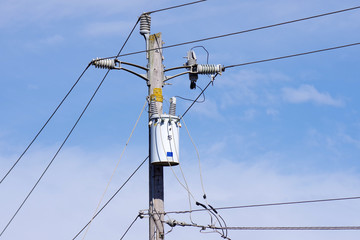 Close view of the top of a electricity distribution pole with power lines and isolators and a...