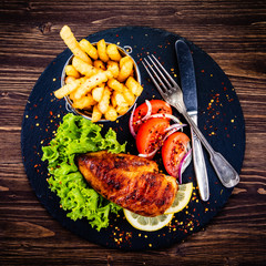 Grilled chicken fillet with french fries on wooden table