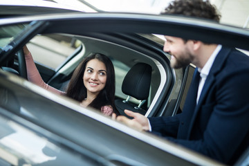 Obraz na płótnie Canvas Elegant woman sitting in car and listening to salesman in automobile center