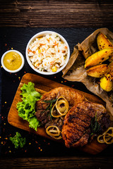 Grilled steak with baked potatoes and vegetables served on black stone plate on wooden table