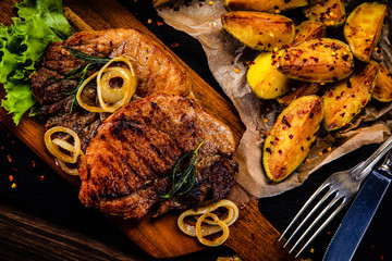 Grilled steak with baked potatoes and vegetables served on black stone plate on wooden table