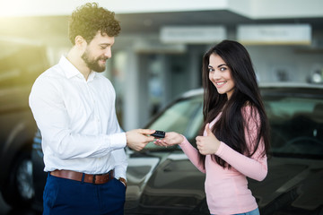 Salesman handing car keys to smiling woman in showroom