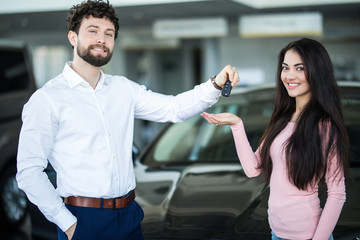 Young oman at a car dealership buying an auto, the sales rep giving her the key
