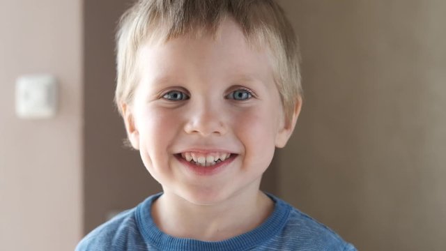 Adorable happy kid baby boy is looking to the camera. Baby looks around and then smiles and laughs. 4 year old fair-haired child with blue eyes smiles at home. Slow motion